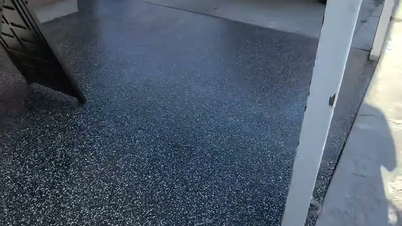 A finished raven flake carport floor with the yard sign standing on it and the street beyond.