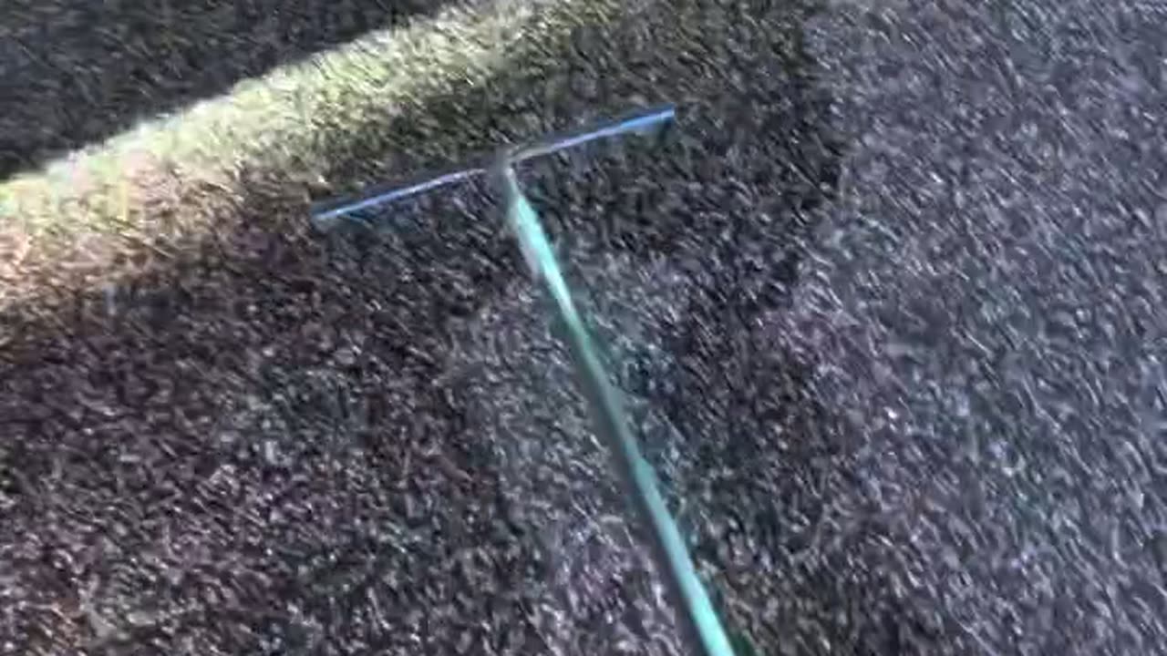 A squeegee pulling clear polyaspartic topcoat across a black and grey flake carport floor.