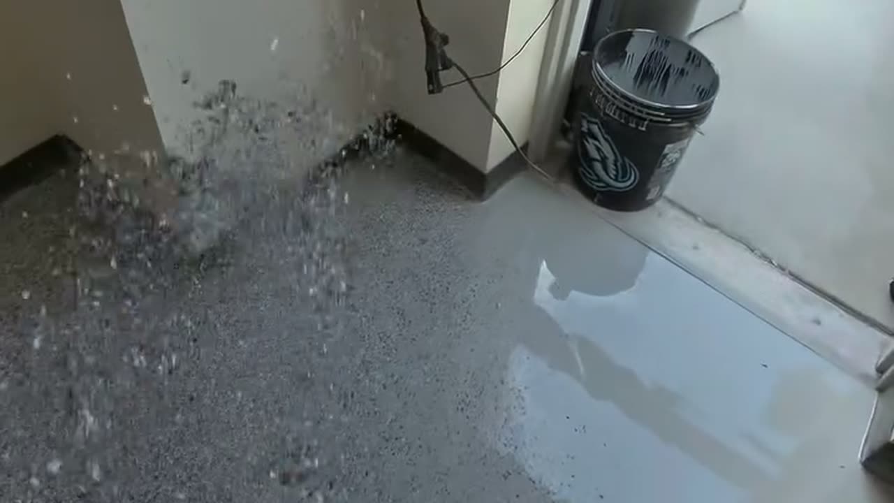 Flake being broadcast by hand across a wet base coat in a shop office, the cabinets and doorway behind.