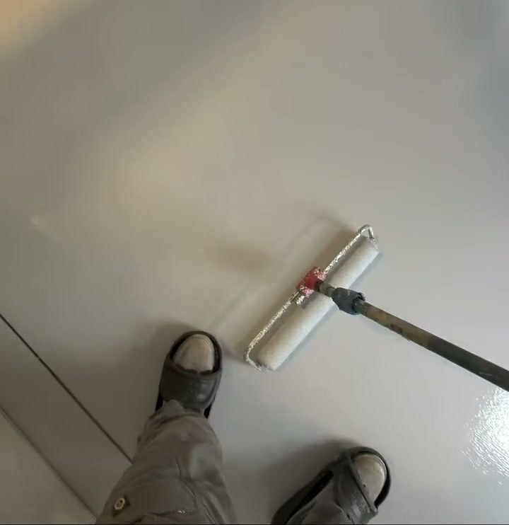 An installer rolling epoxy across an interior room floor at a West Valley City tint shop.