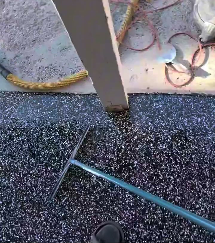 A squeegee pulling clear polyaspartic topcoat across a black and grey flake floor.